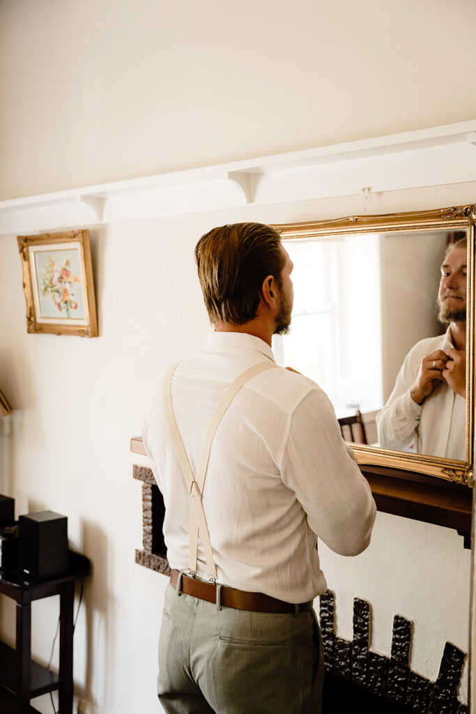 Groom buttons up his shirt, getting ready for his wedding